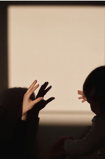 Schaduw van een ouderhand en een kinderhandje op een zonnige muur
