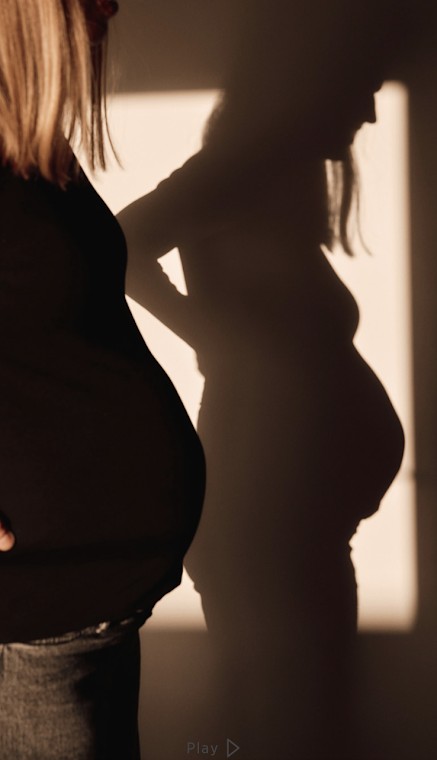 Silhouet van een zwangere vrouw in zacht zonlicht met schaduw op de muur